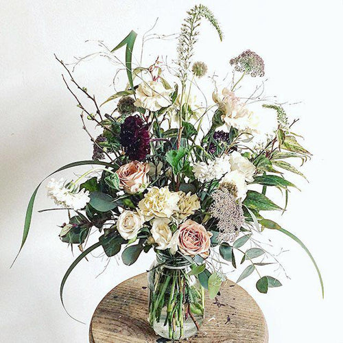 A seasonal spring flower bouquet bursting with flowers in dusky cappuccino, tan and white shades with pops of burgundy and lots of textures and greenery.