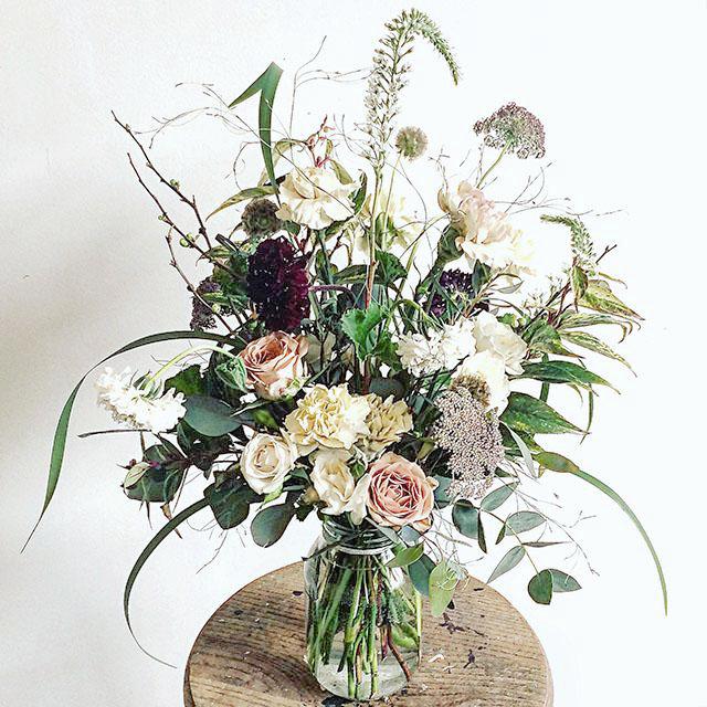 A seasonal spring flower bouquet bursting with flowers in dusky cappuccino, tan and white shades with pops of burgundy and lots of textures and greenery.