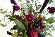 A bouquet bursting with seasonal flowers and foliage in green and burgundy shades with lots of seasonal foliage and texture.
