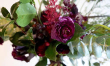 A bouquet bursting with seasonal flowers and foliage in green and burgundy shades with lots of seasonal foliage and texture.