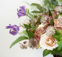 A bouquet full of roses in varying shades of pink, lilac clematis and other summer flowers and foliage.