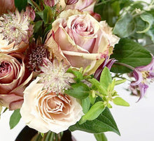 A bouquet full of roses in varying shades of pink, lilac clematis and other summer flowers and foliage.