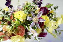 An arrangement bursting with seasonal flowers and foliage and is designed in a lush, asymmetric and horizontal style.  