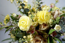 A hand-tied bouquet bursting with seasonal flowers and foliage in shades of yellow and lilac with lots of seasonal greenery and foliages and loads of texture