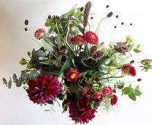 A bouquet full of seasonal flowers in shades of magenta and pink with lots of greenery and texture.