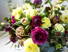 A hand-tied bouquet bursting with seasonal flowers and foliage in shades of yellow, scarlet and dusky pink with lots of seasonal greenery and foliages and loads of texture