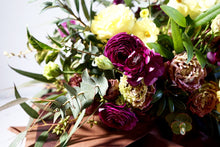 A hand-tied bouquet bursting with seasonal flowers and foliage in shades of yellow, scarlet and dusky pink with lots of seasonal greenery and foliages and loads of texture