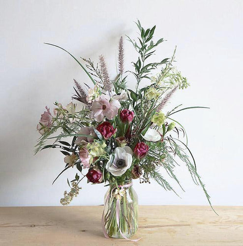A bouquet bursting with seasonal spring flowers in a pink, white and magenta color palette with lots of different foliages. 