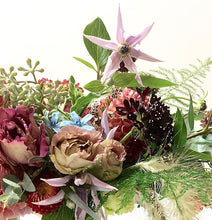 An arrangement bursting with seasonal flowers and foliage designed in a low and horizontal style. 