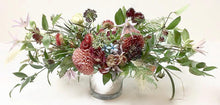 An arrangement bursting with seasonal flowers and foliage designed in a low and horizontal style. 