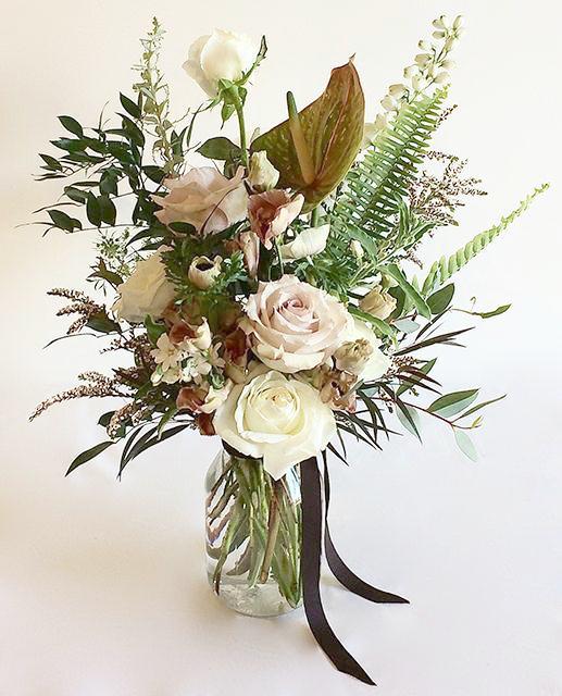 A flower jar bouquet full of seasonal flowers in a white and pastel pink color palette with bursts of greenery and lots of texture.