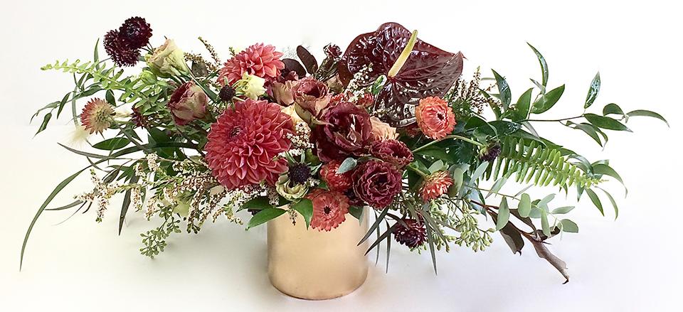 An arrangement bursting with seasonal flowers and foliage and is designed in a low and horizontal style. It makes a perfect gift and is ideal as a table centerpiece. 