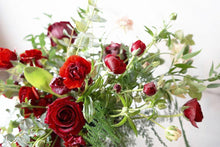 A red rose Valentine's bouquet but with a twist! It is bursting with seasonal flowers and foliage in shades of red and hints of blush with lots of seasonal greenery and foliages and loads of texture. 