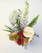 A flower jar bouquet full of seasonal summer flowers in a peach, coral and rusty pink/orange color palette with pops of blue and striking greenery.