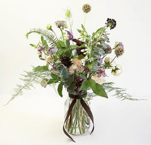 A delicate and airy flower jar bouquet full of seasonal summer flowers in a lilac and pale pink color palette with bursts of greenery and lots of texture. 