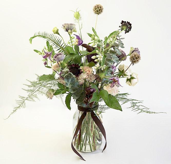 A delicate and airy flower jar bouquet full of seasonal summer flowers in a lilac and pale pink color palette with bursts of greenery and lots of texture. 