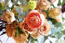 A bouquet bursting with seasonal flowers and foliage in shades of coral and tan with lots of seasonal greenery and foliages and loads of texture.