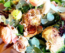 A bouquet bursting with seasonal flowers and foliage in shades of coral and tan with lots of seasonal greenery and foliages and loads of texture.