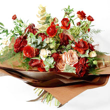 A bouquet bursting with seasonal flowers and foliage in shades of red and tan/cappuccino with lots of seasonal greenery and foliages and loads of texture.   This is not your average red rose Valentine's bouquet but perfect for those who love a little red!
